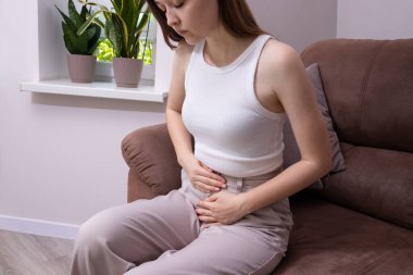 Karın ağrısı, adet sancısı, regl sancısı, şişkinlik, mide bulantısı, yorgunluk ve bel krampları çeken yorgun bir kadın. Adet sağlığı, dönem ağrısı ve regl öncesi sendromu kavramı.