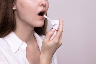 Boğazı ağrıyan bir kadın boğaz spreyi sürüyor. Boğaz ağrısı, grip ve soğuk tedavi kavramı.