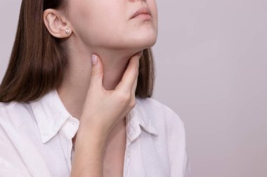 Boğazına dokunan, boğazı ağrıyan, yutkunan bir kadının yakın çekimi. Soğuk algınlığı, grip ya da boğaz enfeksiyonu belirtileri.