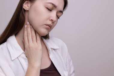 Boynuna dokunan kadın boğaz ağrısı çekiyor, yutkunuyor. Soğuk algınlığı, grip ya da boğaz enfeksiyonu belirtileri.