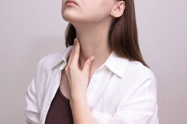 Boğaz bölgesine dokunan kadının tiroid bezini kontrol ettiği yakın plan. Tiroit taraması, tiroid öz muayene, endokrin sağlık....