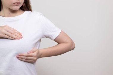 Beyaz tişörtle evde göğüs muayenesi yapan bir kadın. Kendini kontrol etme, meme kontrolü, göğüs kanseri önleme, meme kanseri farkındalığı.