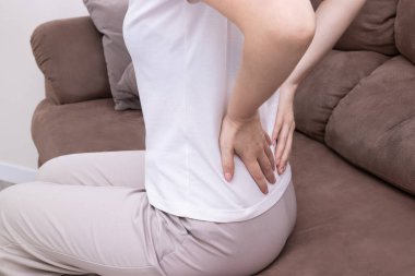 Masaj yapan, koltukta otururken acı veren alt omurgasını ovuşturan bir kadın. Kronik sırt ağrısı, yerleşik yaşam tarzı, omurga gerilimi..