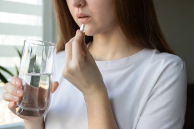 Beslenme takviyeleri. Kadının D vitamini, C vitamini ve bir bardak suyla magnezyum hapı aldığı yakın plan. Günlük sağlık rutini
