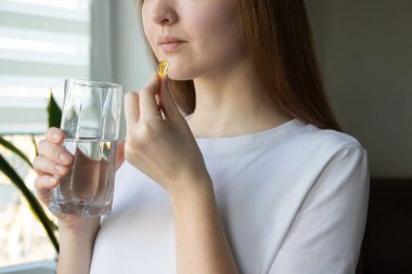 Omega-3, omega-6, omega-9, bir bardak su ile balık yağı kapsülü alan bir kadın. Günlük sağlık rutini