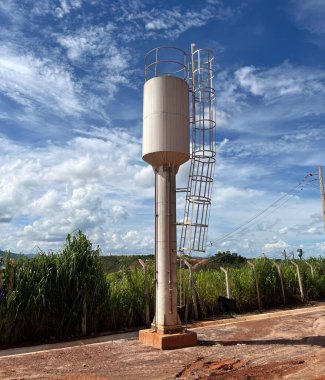 Cup-type water tank with dry column, white in color and installed in front of a fence