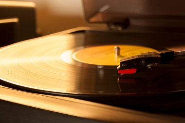 Vinil kayıt ve üreme iğnesinin detayları. Altın ışığın parıltısı diskin bir kısmına yansıyor. Müzik konsepti. Vinil konsepti