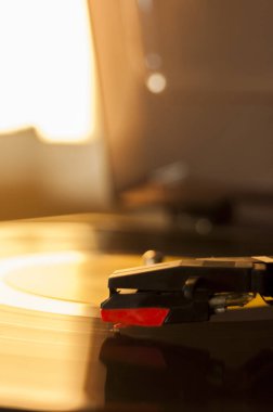 Vinil kayıt ve üreme iğnesinin detayları. Altın ışığın parıltısı diskin bir kısmına yansıyor. Müzik konsepti. Vinil konsepti