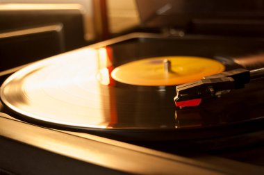 Vinil kayıt ve üreme iğnesinin detayları. Altın ışığın parıltısı diskin bir kısmına yansıyor. Müzik konsepti. Vinil konsepti