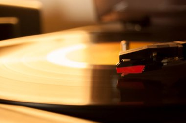 Vinil kayıt ve üreme iğnesinin detayları. Altın ışığın parıltısı diskin bir kısmına yansıyor. Müzik konsepti. Vinil konsepti