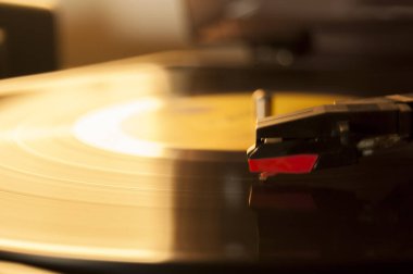 Vinil kayıt ve üreme iğnesinin detayları. Altın ışığın parıltısı diskin bir kısmına yansıyor. Müzik konsepti. Vinil konsepti