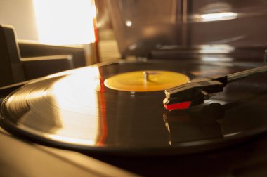 Vinil kayıt ve üreme iğnesinin detayları. Altın ışığın parıltısı diskin bir kısmına yansıyor. Müzik konsepti. Vinil konsepti