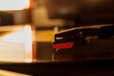 Vinil kayıt ve üreme iğnesinin detayları. Altın ışığın parıltısı diskin bir kısmına yansıyor. Müzik konsepti. Vinil konsepti