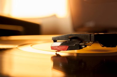 Vinil kayıt ve üreme iğnesinin detayları. Altın ışığın parıltısı diskin bir kısmına yansıyor. Müzik konsepti. Vinil konsepti