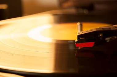 Vinil kayıt ve üreme iğnesinin detayları. Altın ışığın parıltısı diskin bir kısmına yansıyor. Müzik konsepti. Vinil konsepti
