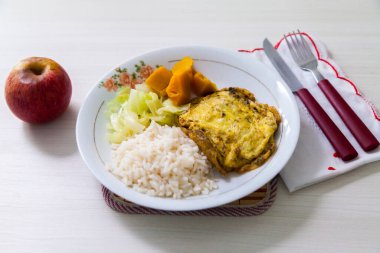 Bir tabak omlet, balkabağı ve lahana, yemek artığı ve tatlı olarak da çatal bıçak ve elma. Brezilya mutfağında beyaz ahşap arka plan, üst manzara. Yemek konsepti. Makarna konsepti.