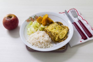 Bir tabak omlet, balkabağı ve lahana, yemek artığı ve tatlı olarak da çatal bıçak ve elma. Brezilya mutfağında beyaz ahşap arka plan, üst manzara. Yemek konsepti. Makarna konsepti.