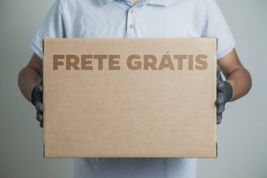 Elinde karton bir kutu tutan siyah eldivenli bir adamın ayrıntıları. Gri arka planda ürünleri teslim etmek için ücretsiz kargo. Teslimat konsepti. Teslimat hizmeti konsepti. Uzayı kopyala Kara Cuma konsepti.