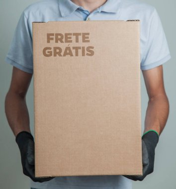 Elinde karton bir kutu tutan siyah eldivenli bir adamın ayrıntıları. Gri arka planda ürünleri teslim etmek için ücretsiz kargo. Teslimat konsepti. Teslimat hizmeti konsepti. Uzayı kopyala Kara Cuma konsepti.