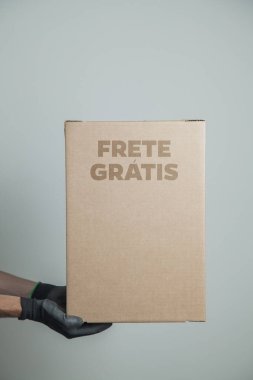 Elinde karton bir kutu tutan siyah eldivenli bir adamın ayrıntıları. Gri arka planda ürünleri teslim etmek için ücretsiz kargo. Teslimat konsepti. Teslimat hizmeti konsepti. Uzayı kopyala Kara Cuma konsepti.