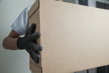 Gri arkaplandaki ürünleri teslim etmek için elinde karton bir kutu tutan siyah eldivenli adamın ayrıntıları. Teslimat konsepti. Teslimat hizmeti konsepti. Boşluğu kopyala.