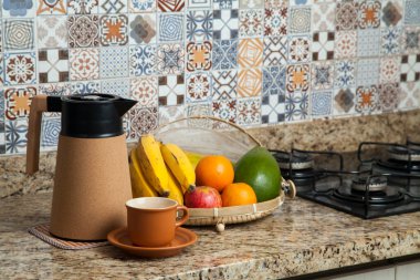 Brezilya kahvaltısı. Kahve termoslu kahvaltı masası, fincanlar ve meyveler sepette, muz, portakal, elma ve avokado. Süslü fayansları olan bir mutfakta tipik Brezilya meyveleri. Yiyecek konsepti.