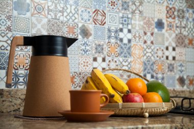 Brezilya kahvaltısı. Kahve termoslu kahvaltı masası, fincanlar ve meyveler sepette, muz, portakal, elma ve avokado. Süslü fayansları olan bir mutfakta tipik Brezilya meyveleri. Yiyecek konsepti.