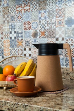 Brezilya kahvaltısı. Kahve termoslu kahvaltı masası, fincanlar ve meyveler sepette, muz, portakal, elma ve avokado. Süslü fayansları olan bir mutfakta tipik Brezilya meyveleri. Yiyecek konsepti.