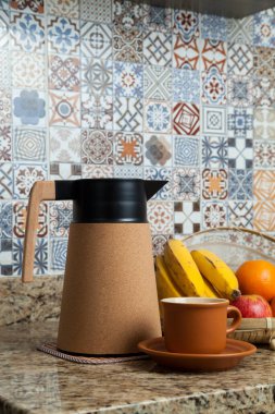 Brezilya kahvaltısı. Kahve termoslu kahvaltı masası, fincanlar ve meyveler sepette, muz, portakal, elma ve avokado. Süslü fayansları olan bir mutfakta tipik Brezilya meyveleri. Yiyecek konsepti.