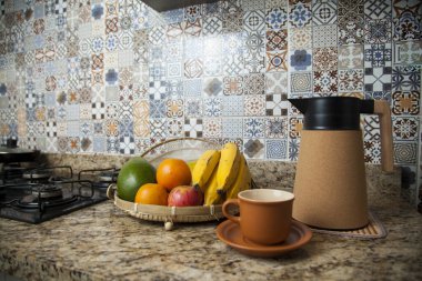 Brezilya kahvaltısı. Kahve termoslu kahvaltı masası, fincanlar ve meyveler sepette, muz, portakal, elma ve avokado. Süslü fayansları olan bir mutfakta tipik Brezilya meyveleri. Yiyecek konsepti.