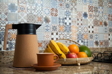 Brezilya kahvaltısı. Kahve termoslu kahvaltı masası, fincanlar ve meyveler sepette, muz, portakal, elma ve avokado. Süslü fayansları olan bir mutfakta tipik Brezilya meyveleri. Yiyecek konsepti.