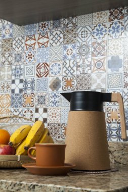 Brezilya kahvaltısı. Kahve termoslu kahvaltı masası, fincanlar ve meyveler sepette, muz, portakal, elma ve avokado. Süslü fayansları olan bir mutfakta tipik Brezilya meyveleri. Yiyecek konsepti.