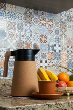 Brezilya kahvaltısı. Kahve termoslu kahvaltı masası, fincanlar ve meyveler sepette, muz, portakal, elma ve avokado. Süslü fayansları olan bir mutfakta tipik Brezilya meyveleri. Yiyecek konsepti.