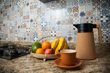 Brezilya kahvaltısı. Kahve termoslu kahvaltı masası, fincanlar ve meyveler sepette, muz, portakal, elma ve avokado. Süslü fayansları olan bir mutfakta tipik Brezilya meyveleri. Yiyecek konsepti.