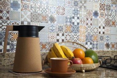 Brezilya kahvaltısı. Kahve termoslu kahvaltı masası, fincanlar ve meyveler sepette, muz, portakal, elma ve avokado. Süslü fayansları olan bir mutfakta tipik Brezilya meyveleri. Yiyecek konsepti.