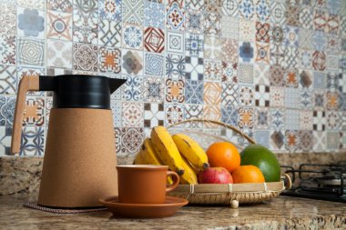 Brezilya kahvaltısı. Kahve termoslu kahvaltı masası, fincanlar ve meyveler sepette, muz, portakal, elma ve avokado. Süslü fayansları olan bir mutfakta tipik Brezilya meyveleri. Yiyecek konsepti.