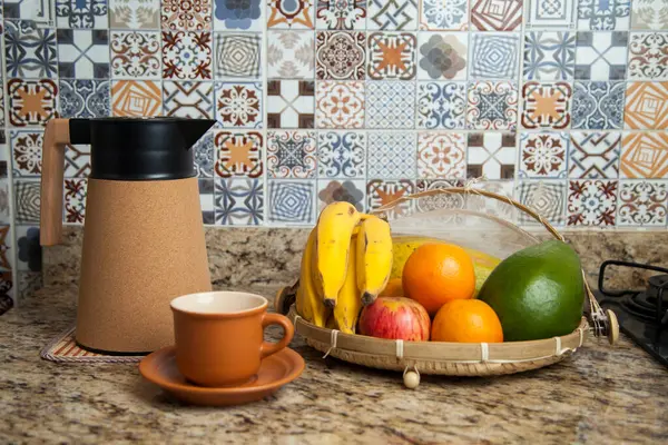 Brezilya kahvaltısı. Kahve termoslu kahvaltı masası, fincanlar ve meyveler sepette, muz, portakal, elma ve avokado. Süslü fayansları olan bir mutfakta tipik Brezilya meyveleri. Yiyecek konsepti.