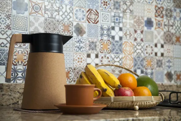 Brezilya kahvaltısı. Kahve termoslu kahvaltı masası, fincanlar ve meyveler sepette, muz, portakal, elma ve avokado. Süslü fayansları olan bir mutfakta tipik Brezilya meyveleri. Yiyecek konsepti.