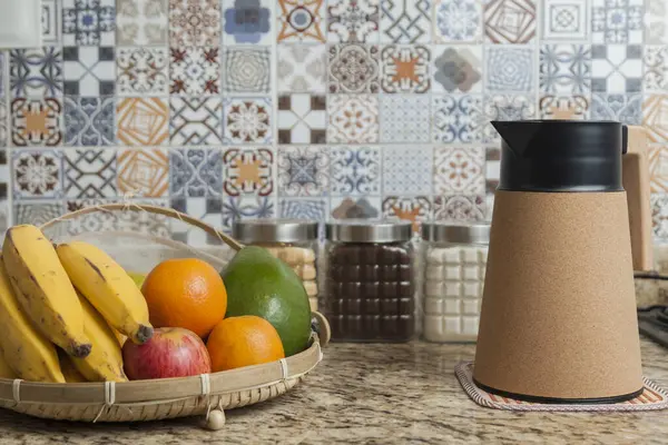 Kahve termosu, fincan ve kavanoz şeker, kahve, muz, elma, portakal ve avokado içeren Brezilya kahvaltı masası. Arka planda fayanslarla süslenmiş tipik Brezilya mutfağı. Yiyecek konsepti.