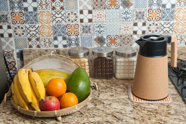Kahve termosu, fincan ve kavanoz şeker, kahve, muz, elma, portakal ve avokado içeren Brezilya kahvaltı masası. Arka planda fayanslarla süslenmiş tipik Brezilya mutfağı. Yiyecek konsepti.