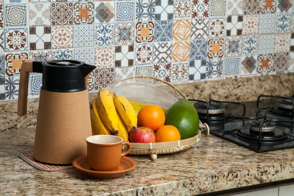 Brezilya kahvaltısı. Kahve termoslu kahvaltı masası, fincanlar ve meyveler sepette, muz, portakal, elma ve avokado. Süslü fayansları olan bir mutfakta tipik Brezilya meyveleri. Yiyecek konsepti.