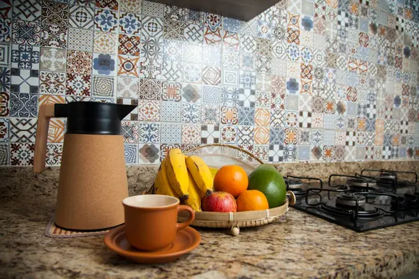 Brezilya kahvaltısı. Kahve termoslu kahvaltı masası, fincanlar ve meyveler sepette, muz, portakal, elma ve avokado. Süslü fayansları olan bir mutfakta tipik Brezilya meyveleri. Yiyecek konsepti.