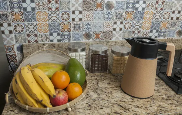 Kahve termosu, fincan ve kavanoz şeker, kahve, muz, elma, portakal ve avokado içeren Brezilya kahvaltı masası. Arka planda fayanslarla süslenmiş tipik Brezilya mutfağı. Yiyecek konsepti.