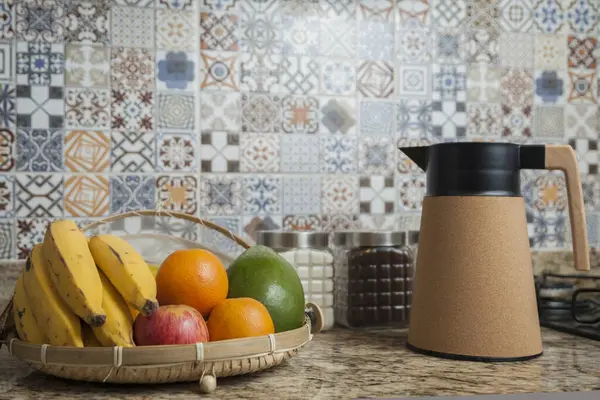 Kahve termosu, fincan ve kavanoz şeker, kahve, muz, elma, portakal ve avokado içeren Brezilya kahvaltı masası. Arka planda fayanslarla süslenmiş tipik Brezilya mutfağı. Yiyecek konsepti.