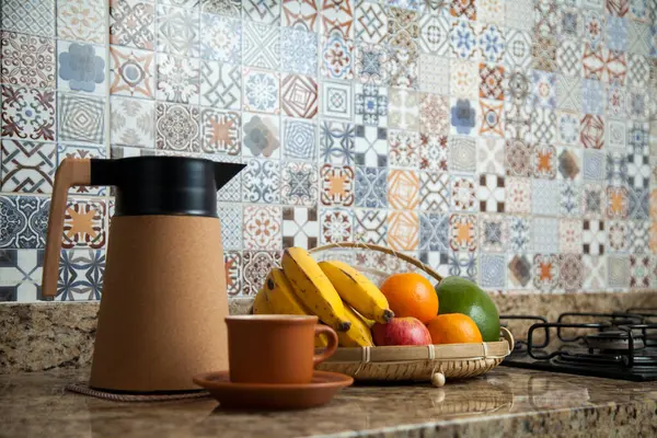 Brezilya kahvaltısı. Kahve termoslu kahvaltı masası, fincanlar ve meyveler sepette, muz, portakal, elma ve avokado. Süslü fayansları olan bir mutfakta tipik Brezilya meyveleri. Yiyecek konsepti.