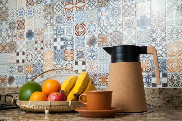 Brezilya kahvaltısı. Kahve termoslu kahvaltı masası, fincanlar ve meyveler sepette, muz, portakal, elma ve avokado. Süslü fayansları olan bir mutfakta tipik Brezilya meyveleri. Yiyecek konsepti.
