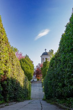 Yoğun çitlerle kaplı sakin bir patika huzurlu bir bahçe ortamında güzel bir çan kulesine çıkıyor. Açık mavi gökyüzü manzaranın huzurlu atmosferini arttırır..