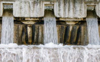 Beton barajın birçok çıkışından nehre dökülen su köpük ve su sıçramasına neden oluyor. Sahne, sakin bir manzarada akan suyun doğal güzelliğini yakalar..
