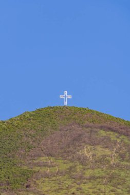 Büyük beyaz bir haç yeşil bir dağın tepesinde canlı mavi bir gökyüzünün altında dimdik duruyor. Haçın etrafındaki manzara yeşil tepeler ve çorak arazilerin karışımını içeriyor. Bu da yeni havanın değiştiğini gösteriyor..