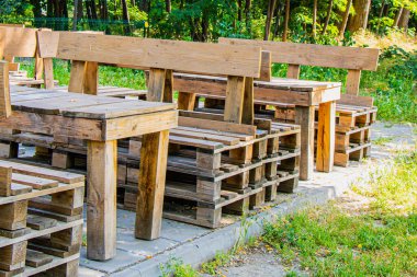 Paletlerden yapılan el yapımı ahşap banklar ve masalar yeşil çimenler ve ağaçlarla çevrili güneşli bir açık alanda düzenlenir. Bu ayar rahatlama ve toplantıları davet eder.
